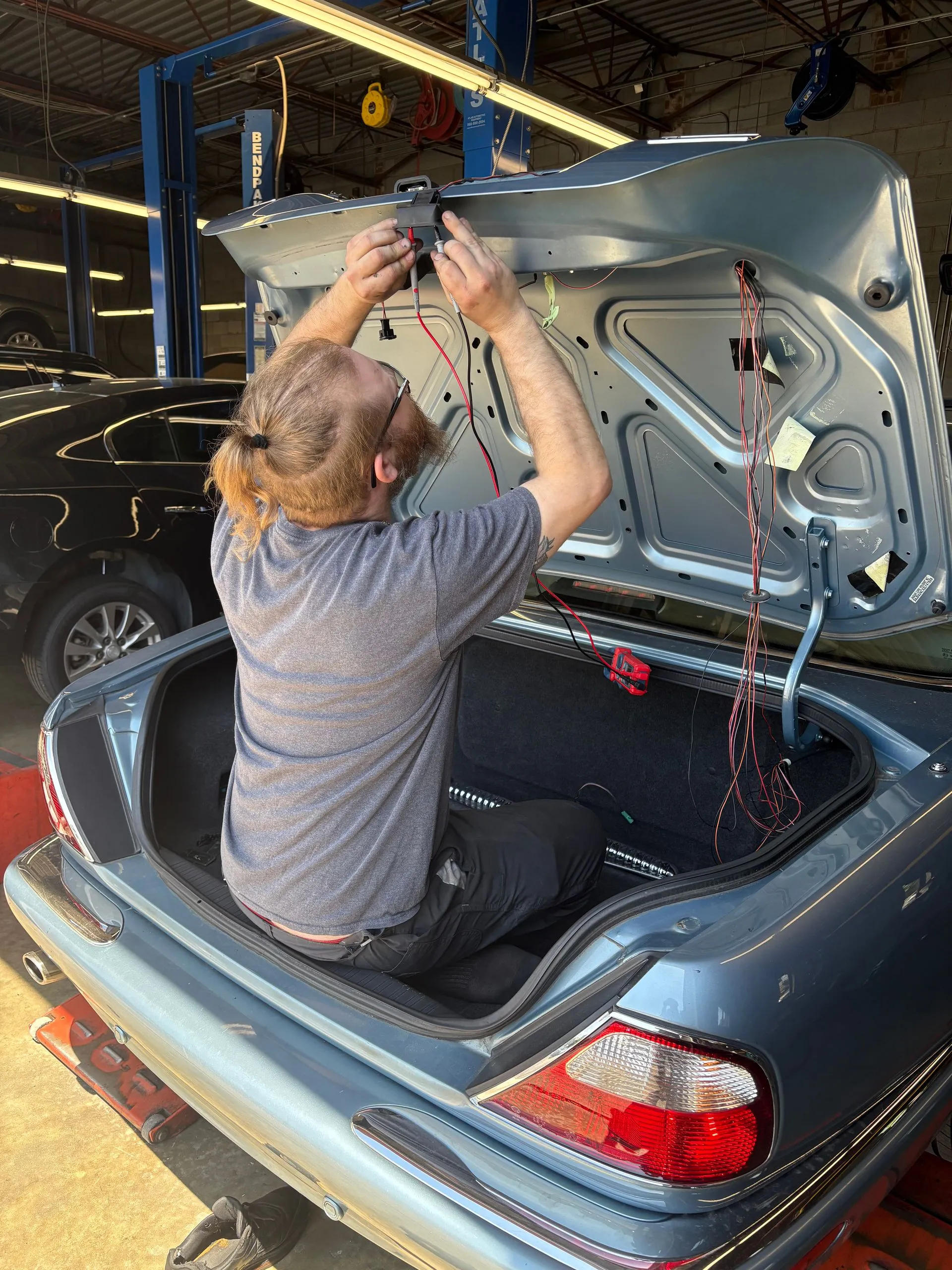 Person installing a trunk lid on a dark car in the garage