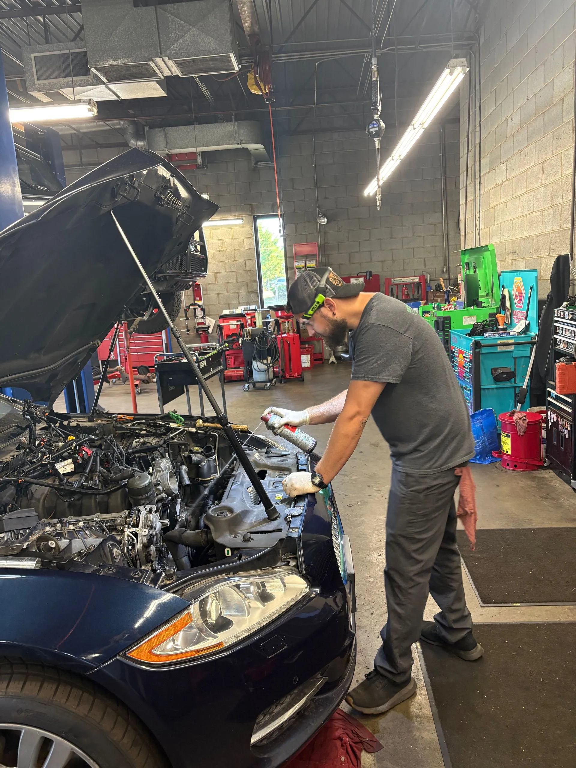 Mechanic inspecting a vehicle with its hood open inside the shop